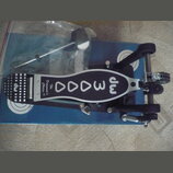 Černý basový pedál s kovovými prvky a bílým nápisem na šlapce. Na šlapce je zrcadlově otočený nápis „The Drummer's Choice“ a logo „dw“. Pedál leží na…