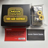 Na fotografii je kytarový efekt v plastovém obalu, černá krabice a dva doprovodné papíry. Na krabici je žlutý nápis MXR CUSTOM SHOP X THIRD MAN HARDW…