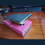 Růžový wah-wah pedál s černým gumovým nášlapem a chromovaným okrajem. Na pravém boku je viditelný nápis „George Dennis“ a pod ním menší text „CUSTOM…