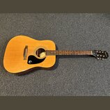 Akustická kytara s přírodním dřevem, tmavě hnědými boky a černým plechtřem. Na hlavě hmatníku je bílý nápis Epiphone. Uvnitř ozvučovacího otvoru je v…