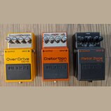 Tři kytarové efekty značky BOSS v žluté, oranžové a černé barvě. Horní pedál má nápisy OverDrive OP-1X, prostřední Distortion DS-1X a spodní Metal Zo…