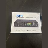 Fotografie znázorňuje krabici od USB audio rozhraní. Na krabici je velký modrý nápis M4 a text 4-in / 4-out USB audio interface with studio-quality s…