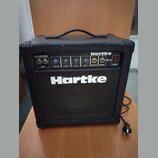 Černý basový kombozesilovač s nápisy Hartke a B200. Horní ovládací panel obsahuje vstup INPUT s přepínačem PASSIVE/ACTIVE, čtyři modré otočné ovladač…