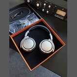 Stříbrná studiová sluchátka s černým náušníkem v oranžovo-černé krabici. Na obou mušlích je nápis STUDIO HEADPHONE 600 a BEHMANN BERLIN. Vedle sluchá…