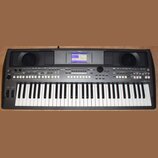 Šedý digitální klavír s nápisem YAMAHA v horní části. V pravém dolním rohu je označení modelu PSR-S570. Nástroj má vestavěný displej, dvě mřížky repr…