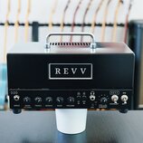 Černý kytarový zesilovač s kovovou rukojetí nahoře. Na předním panelu je bílý obdélníkový štítek s nápisem REVV a vlevo označení D20. Panel obsahuje…