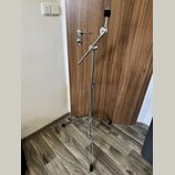 Stříbrný kovový mikrofonní stojan s trojnožkou. Stojan má teleskopický středový sloup a vyklápěcí rameno s černým držákem v horní části. Povrch je le…