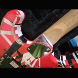 Detail zadní části těla a krku elektrické kytary s červeno-bílo-černým vzorem Union Jack. Na těle jsou vidět výrazné odrolení laku a odštípnuté části…