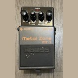 Černý kytarový efekt pedál značky BOSS, model Metal Zone MT-2. Horní část obsahuje čtyři ovládací knoflíky s popisky MIN MAX, -15 HIGH +15 LOW a 200…