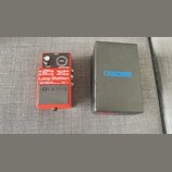 Červený efekt pedál s nápisy Loop Station, RC-1 a BOSS. Na horní části jsou ovládací prvky: knoflík LEVEL, kontrolka CHECK a spínač STOP/UNDO. Na pře…