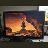 Na fotografii je černý monitor nebo televize značky SAMSUNG. Displej zobrazuje tapetu s krajinou, čas 11:13 a datum pondělí 6. července. Zařízení je…
