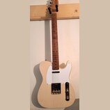Elektrická kytara typu Telecaster s přírodním dřevěným povrchem těla a hmatníkem. Má bílý pickguard, jeden krkový snímač a jeden mostový snímač v kov…