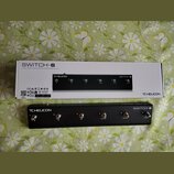 Černý kontrolní pedál s nápisy TC HELICON a SWITCH-6. Zařízení obsahuje šest stomečových spínačů s označením čísel 1 až 6 a doplňkovými nápisy HIT, P…