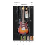Elektrická kytara s trupem v barevnosti sunburst a tmavě červeným pickguardem s bílými vlożkami. Nástroj leží v černém polstvu, vedle něj jsou přilož…