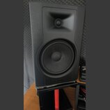 Černý studiový monitor s dvěma reproduktory umístěný na černém stojanu. V dolní části přední mřížky je vyražen nápis M-AUDIO BX. Povrch je matný, s v…