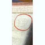 Detailní záběr na stříbrný kovový povrch s viditelnými škrábanci a opotřebením. V červeném kruhu je vyrytý, velmi nečitelně působící nápis nebo logo.…
