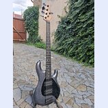 Elektrická basová kytara s tmavě šedým trpytivým povrchem těla a hnedým dřevěným hmatníkem a hlavou. Na hlavě je svisle napsaný nápis Ibanez. Tělo má…
