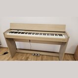 Digitální piano v dřevěném provedení světlé barvy s integrovaným stojanem a třemi pedály. Na pravém boku korpusu je viditelné logo Roland. Nástroj má…
