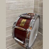 Hnědý dřevěný buben s chromovaným kováním a bílým blátcem. Na korpusu je čtvercový štítek s nápisy „Pearl“, „Master's Idea“ a „Hand-selected Mahogany…