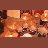 bicí souprava v červeném metallic provedení s kovovým kováním. Na činelech je vidět nápis pAiste, na bubnůvých blanách je logo s nápisem Pearl. Soupr…