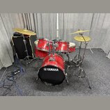 Červená bicí souprava značky YAMAHA s černým předním bendem basového bubnu, na kterém je bílé logo a nápis YAMAHA. Sestava obsahuje basový buben, dva…