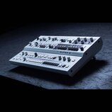 Bílý analogový syntetizátor s výrazným nápisem UDG SUPER 6. Přístroj má rozsáhlý ovládací panel s mnoha posuvníky, otočnými knoflíky a bílými tlačítk…