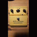 Žlutý kytarový efekt pedál s kovovým tělem. Na přední straně jsou tři černé oválné knofíky s popisky LEVEL, DRIVE a PRE-BASS, přepínač ON a nápisy OU…