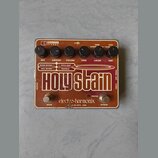 Efektový pedál v hnědo-oranžové barvě s nápisem Holy Stain. Na horní části jsou šest černých otočných ovladačů s popisky MIX, AMOUNT, VOLUME, TONE, C…