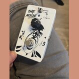 Bílý efekt pedál s černým grafickým motivem a nápisem THE NOISE. Na horní části je přepínač s popisky HARD a SOFT a nápis Ca dine. Uprostřed se nachá…