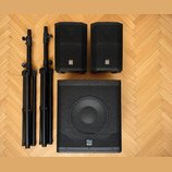 Dva černé reproduktory s logem Ey a jeden větší černý subwoofer s logem KALI. Soubor doplňují dva černé rozkládací reproduktorové stojany. Všechny ko…