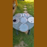 Šest kusů bubnových koží v různých velikostech položených na kulatém plastovém stole. Na kožích jsou vidět nápisy SONOR a REMO. Povrchy jsou průhledn…