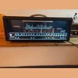 Černý kytarový zesilovač s průhledným předním panelem, skrze který jsou vidět elektronické válvy. Na skle je bílý nápis Hughes & Kettner a vpravo mod…