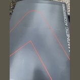 Detailní záběr na šedý povrch s nápisem MAGNETIC ACCESSORIES. Na povrchu jsou vidět tenké červené linky tvořící geometrické tvary. Materiál vykazuje…