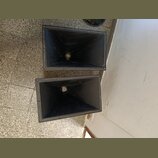 Dvě černé plastové akustické trouby s hranatým tvarem. Povrch je matný a v horní části jsou vidět drobné nečistoty a prach. Na fotce nejsou žádné vid…