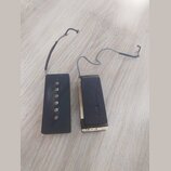Dvě černé kytarové remeny z kůže nebo syntetického materiálu s připevněnými šňůrkami. Levý řemen má v horní části pět kovových nýtů pro nastavení dél…