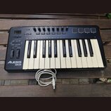 Černý kompaktní MIDI kontrolér s klávesnicí, umístěný na dřevěném stole. Na levé straně je bílý nápis ALESIS QX25 a ovládací prvky v podobě tlačítek,…