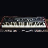 Černý syntetizátor s červenými bočními panely a bílo-černou klaviaturou. V pravém horním rohu je nápis Legend One ANALOG SYNTHESIZER. Horní panel obs…