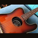 Akustická kytara s barevným přechodem od oranžové k tmavě hnědé (sunburst). Uvnitř ozvučovacího otvoru je štítek s nápisy Fender, Telecoustic, ELECTR…