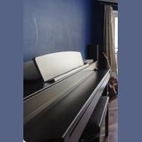Černý digitální piano s doprovodnou stoličkou. Na horní části korpusu je vidět vybledlý nápis YAMAHA. Na nástroji je umístěn bílý notový stojan. V po…
