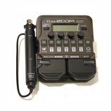 Šedý multifunkční procesor s nápisem A1 FOUR ZOOM Multi-Effects Processor. Zařízení obsahuje displej, ovládací knoflíky a pět stoupacích spínačů s čí…