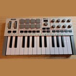 Bílá MIDI klaviatura s názvy AKAI PROFESSIONAL a MPK mini. Horní panel obsahuje šedé čtvercové pady, několik otočných potenciometrů a řadu malých tla…