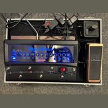 V otevřeném hliníkovém kufru se nachází černý kytarový zesilovač s modře podsvíceným panelem, na kterém je nápis Hughes & Kettner a model Black Spiri…