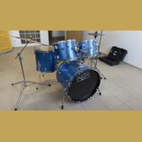 Modrá bicí souprava s kovovými obručemi a chromovaným hardwarem. Na basovém bubnu je nápis TORNADO a pod ním logo MAPEX, stejný název TORNADO je vidě…