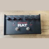 Černý efekt pedál s nápisy DEUCETONE a RAT. Horní panel obsahuje dva identické sady ovládacích prvků s popisky Distortion, Filter a Volume. Ve spodní…