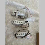 Tři bílé snímače pro elektrickou kytaru, každý zabalený v samostatném průhledném plastovém sáčku. Snímače mají plastové kryty a jsou vybaveny připojo…