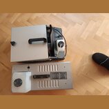 Dvě stříbrné kovové krabice s černými madly, položené na dřevěné podlaze. Horní zařízení má otevřenou boční část, kde je vidět bílá plastová nádoba a…