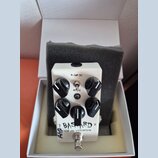 Bílý efekt pedál s nápisy BAS TARD a LOW END DISTORTION v bílé krabičce s šedou pěnovou vložkou. Pedál má čtyři černé oválné ovládací knoflíky, jeden…