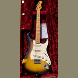 Elektrická kytara typu Stratocaster s barevným přechodem těla od žluté přes hnědou k černé. Na hlavě hmatníku je viditelné logo Fender. Nástroj vykaz…