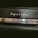 Detail kytarového komba s černým povrchem a stříbrným ovládacím panelem. Na horní části je nápis Hughes & Kettner a vpravo na panelu označení Tube 50…