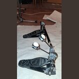 Černý dvojpedál k bicím s kovovými mechanismy a bílými plstěmi na beaterech. Na obou pedálech je nápis IRON COBRA a u levého pedálu je doplněný text…